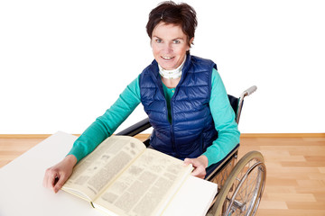 Woman with book sitting in a wheelchair at the table
