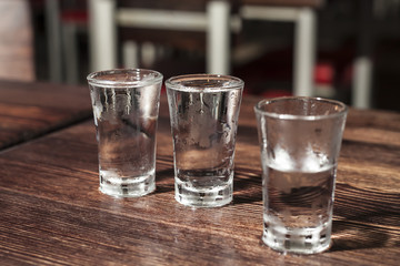 Three frozen shot glasses of vodka on a wooden table.