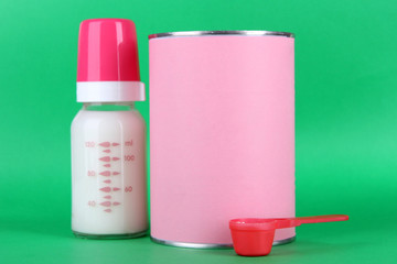 Powdered milk with baby bottle of milk on green background.