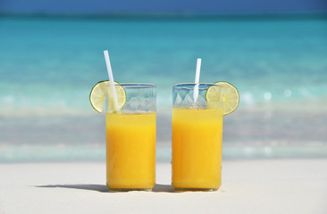Two glasses of orange juice on the sandy beach