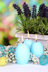 Easter candles with flowers on bright background