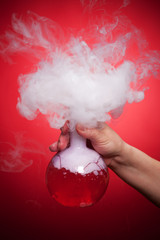 Steaming flask with red liquid in the hand on a red background