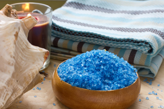 Sea salt in bowl with candle and towels on wooden background