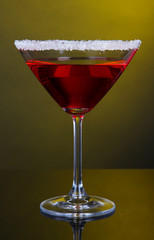 Red cocktail in martini glass on dark yellow background