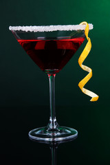 Red cocktail in martini glass on dark green background