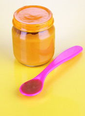 Baby food with weaning spoon on yellow background