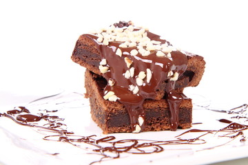 Slices of a brownie on a plate covered with chocolate and nuts