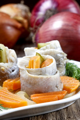 Pickled herring rolls with vegetables on wooden table