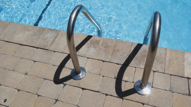 Swimming pool ladder beside clean, summer pool.