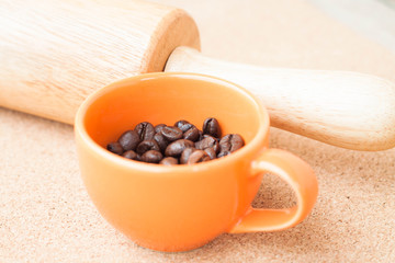 Cup of roast coffee bean and roller on cork background