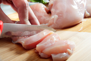Fototapeta Man's hand cutting raw chicken breast obraz