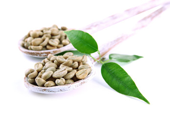 Green coffee beans in wooden spoons and leaves isolated on