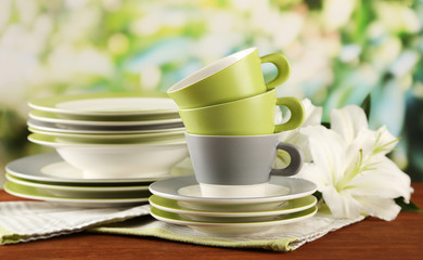 Empty plates and cups on wooden table on green background