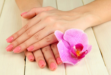 Woman hands with pink manicure and orchid on  wooden background