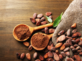 Cocoa powder in spoons and cocoa beans on wooden background