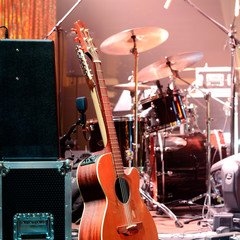 Acoustic guitar, drum kit, loudspeaker and other musical equipment on stage before concert. Red light. Concept image. Night club, performance, music band, singing, profession, art, instrument