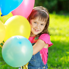 Fototapeta na wymiar Little happy girl holding colorful balloons in green park