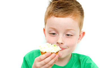 handsome little boy eating a fresh cream cup cake with messy fac