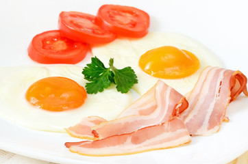 Breakfast with bacon, fried eggs and slices tomatoes
