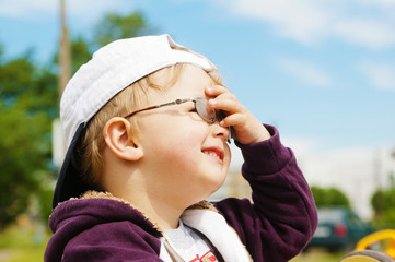 Little boy in glasses hand covers the eyes from bright sun