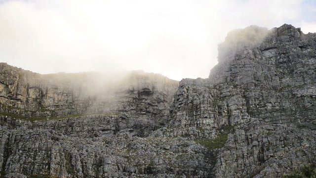 White clouds hanging above grey rocky part of Table Mountain