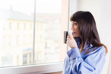 Obraz premium Woman standing by the window drinking coffee