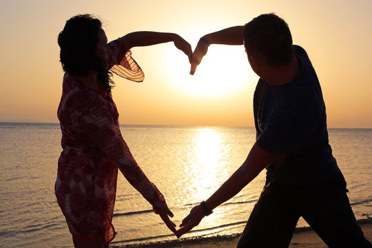 Couple making romantic heart shape at sunrise on the beach