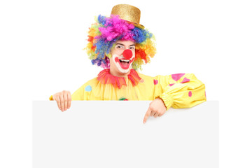 A happy male clown pointing on a blank panel