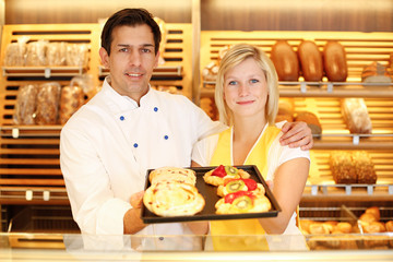 Baker and shopkeeper in bakery with tablet of cake