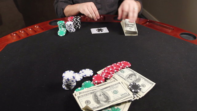 A gambler at a poker table bets some money, lays down a royal flush, then takes the pot.