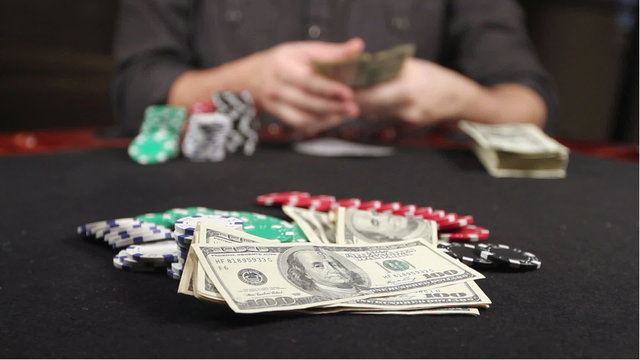 A gambler at a poker table puts his cards down and bets a stack of hundreds.