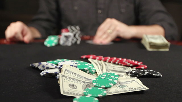 A gambler at a poker table peeks at his cards ‘and bets a stack of chips