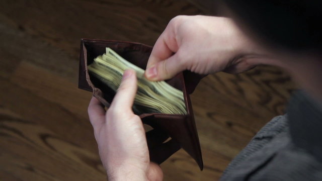 High angle, looking in a man&rsquo;s wallet as he sifts through hundred dollar bills, takes one out, then places it back in.