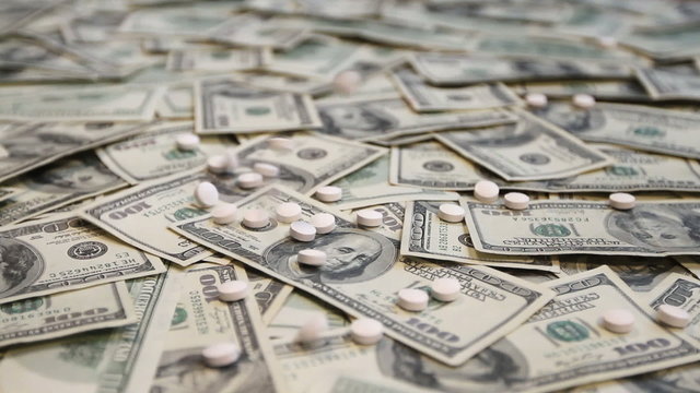 White pills falling onto a pile of hundred dollar bills.