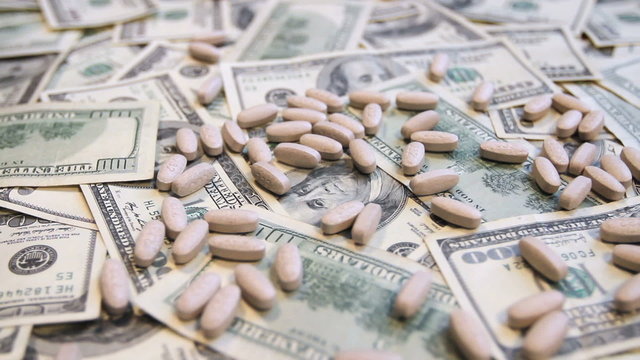 White pills falling onto a pile of hundred dollar bills.