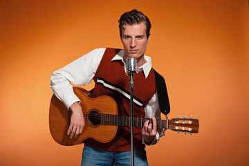 Retro fifties rock and roll singer playing acoustic guitar. Stud