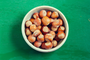 Hazelnuts in ceramic bowl over wooden background