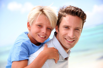 Daddy giving piggyback ride to son by the beach