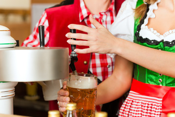 Junge Frau in Tracht zapft ein Bier im Restaurant
