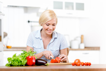 Obraz na płótnie Canvas Woman cuts groceries for salad sitting at the kitchen