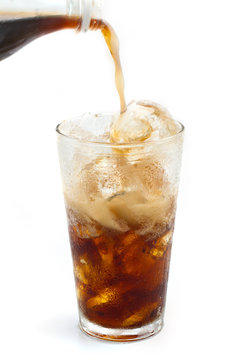 A Bottle of cola soda pouring into a glass filled with ice cubes