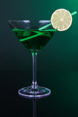Green cocktail in martini glass on dark green background