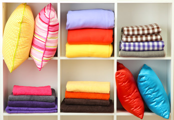 Bright pillows, towels and plaids on shelves, isolated on white