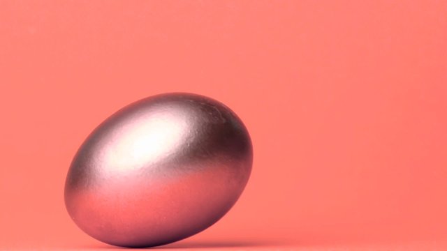 Shiny egg rolling across pink surface