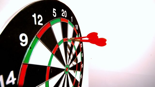 Dart hitting the dart board between two other darts side view