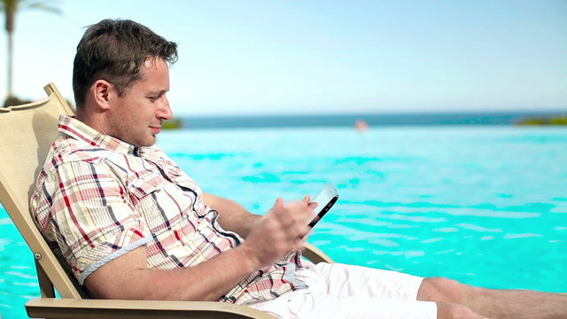 Young man taking photo with tablet by swimming-pool in hotel, st