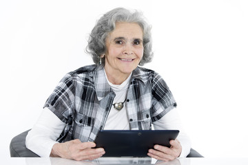 Alte Frau sitzt mit Tablet in der Hand & lächelt  in die Kamera