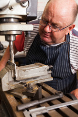 senior man using industrial drilling machine in workshop