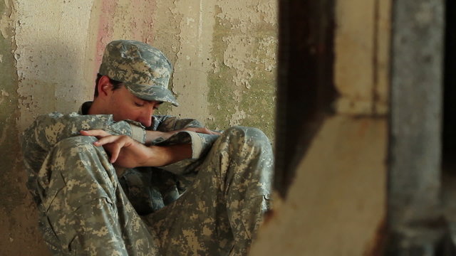 Distraught soldier sitting against concrete wall