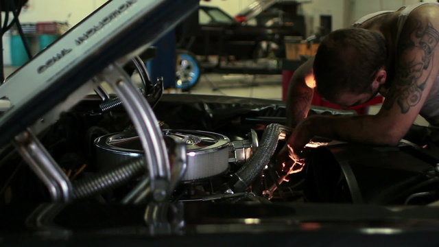 Man working on the engine of a classic car in a shop, dolly shot